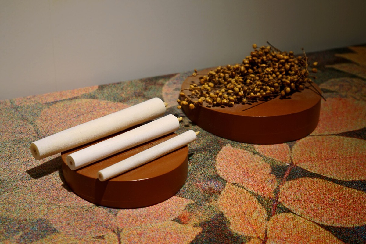 A museum display: three cream-coloured hand-rolled Japanese candles resting on a terracotta disc, beside a second disc heaped with dried urushi berries on their stems.